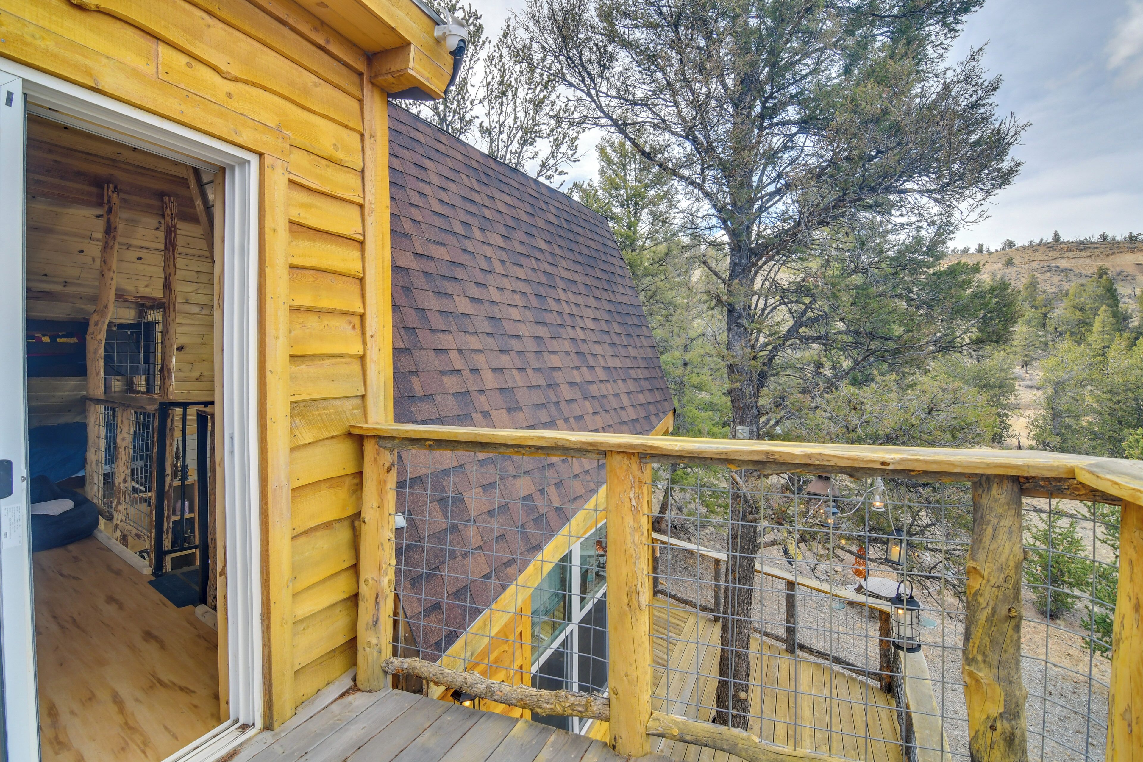 A wooden cabin with a deck, a window, and a view of trees and hills.