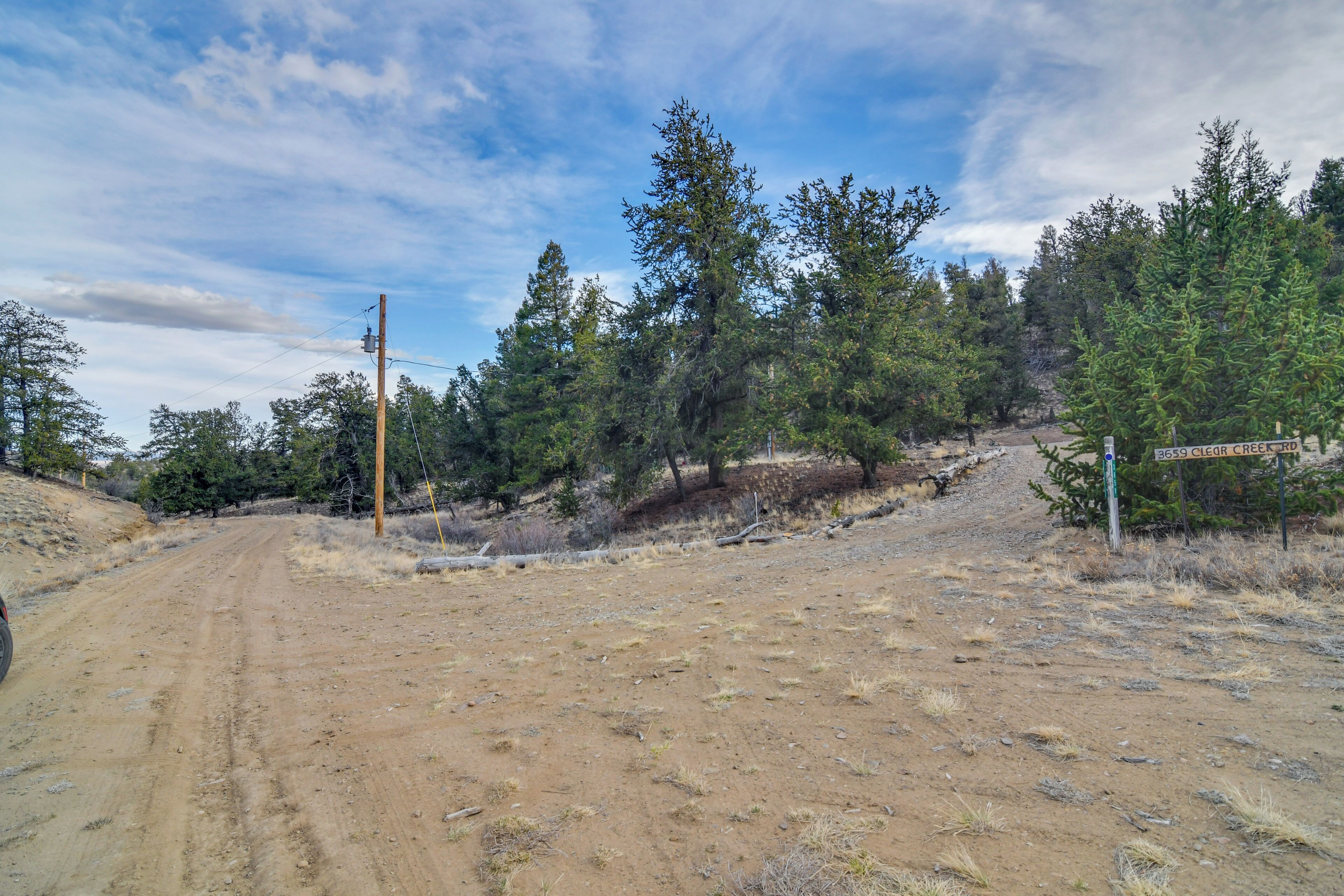 A dirt road leading through a forested area with a sign indicating '3659 Clear Creek Rd.'