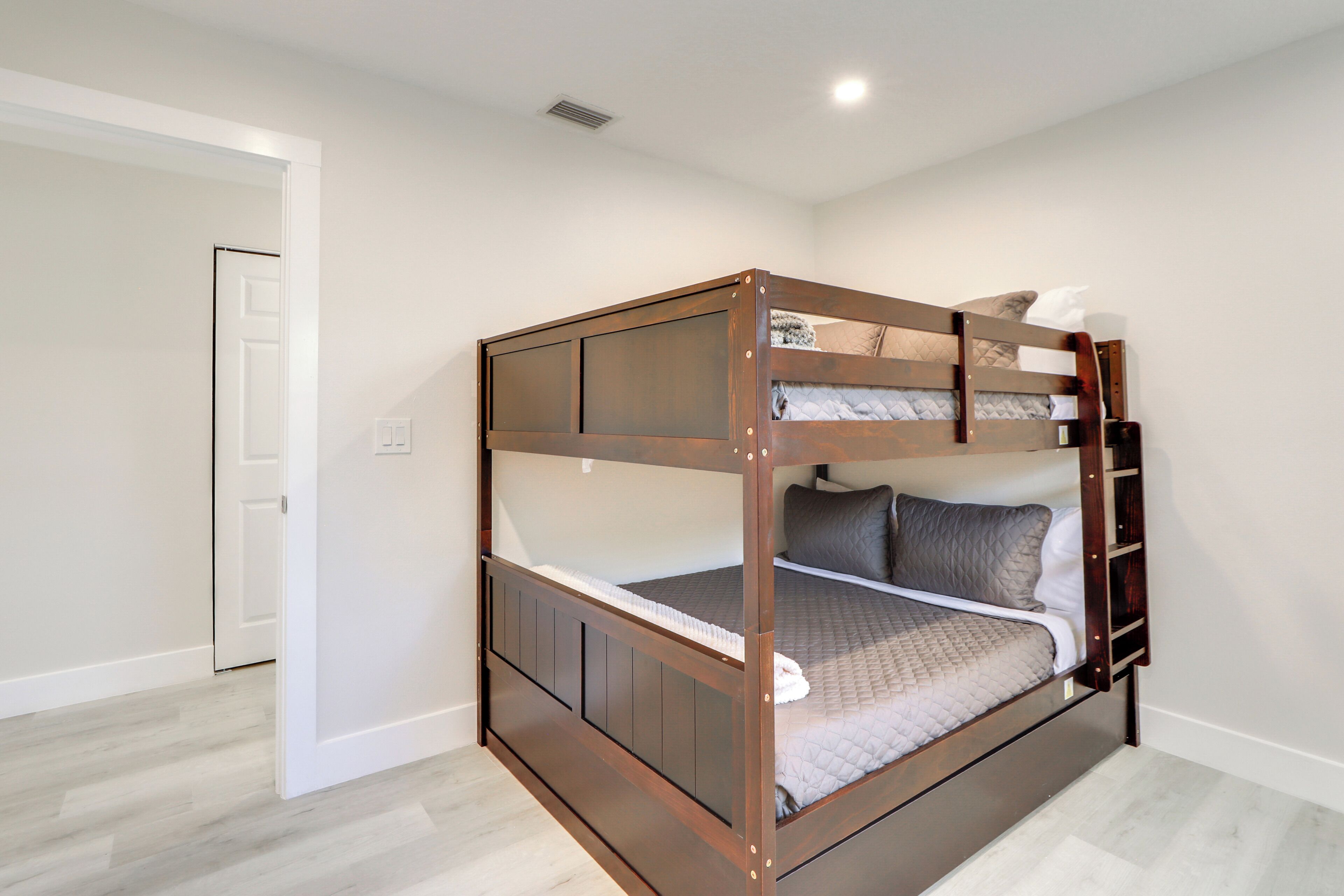 A bunk bed with a ladder, a door, and a light switch on the wall.