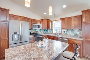 A kitchen with wooden cabinets, stainless steel appliances, granite countertops, and pendant lighting.