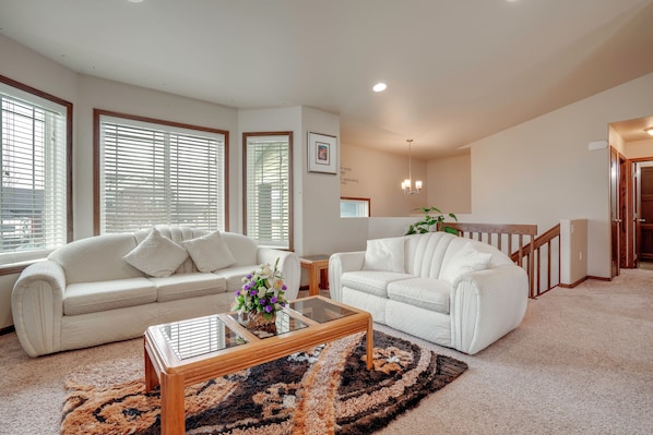 A living room with two white sofas, a glass coffee table, and a patterned rug.