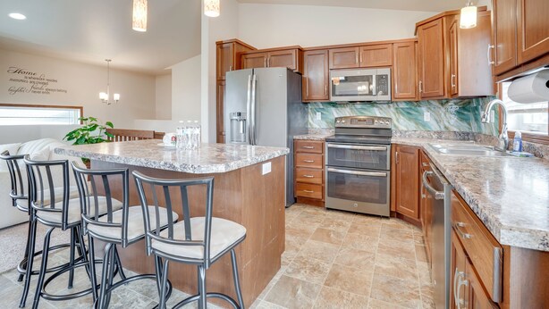 A kitchen with wooden cabinets, stainless steel appliances, a marble backsplash, and a bar area with stools.