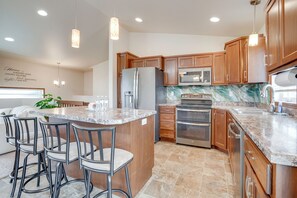 A kitchen with wooden cabinets, stainless steel appliances, a marble backsplash, and a bar area with stools. - Family Friendly! Spacious Moorhead Haven w/ Yard (Moorhead)