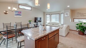 A modern kitchen with granite countertops, a dining area with chairs, a built-in oven, and a living area with a sofa and TV.