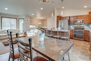 A modern kitchen with stainless steel appliances, a dining area with a glass table, and a living room with a white sofa.