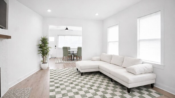 A modern living room with a white sectional sofa, a checkered rug, a dining area with chairs, and a potted plant.