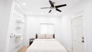 A bedroom with a bed, a ceiling fan, a window, and a door.