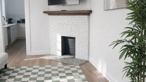 A living room with a checkered rug, a fireplace, a mounted TV, and a potted plant.