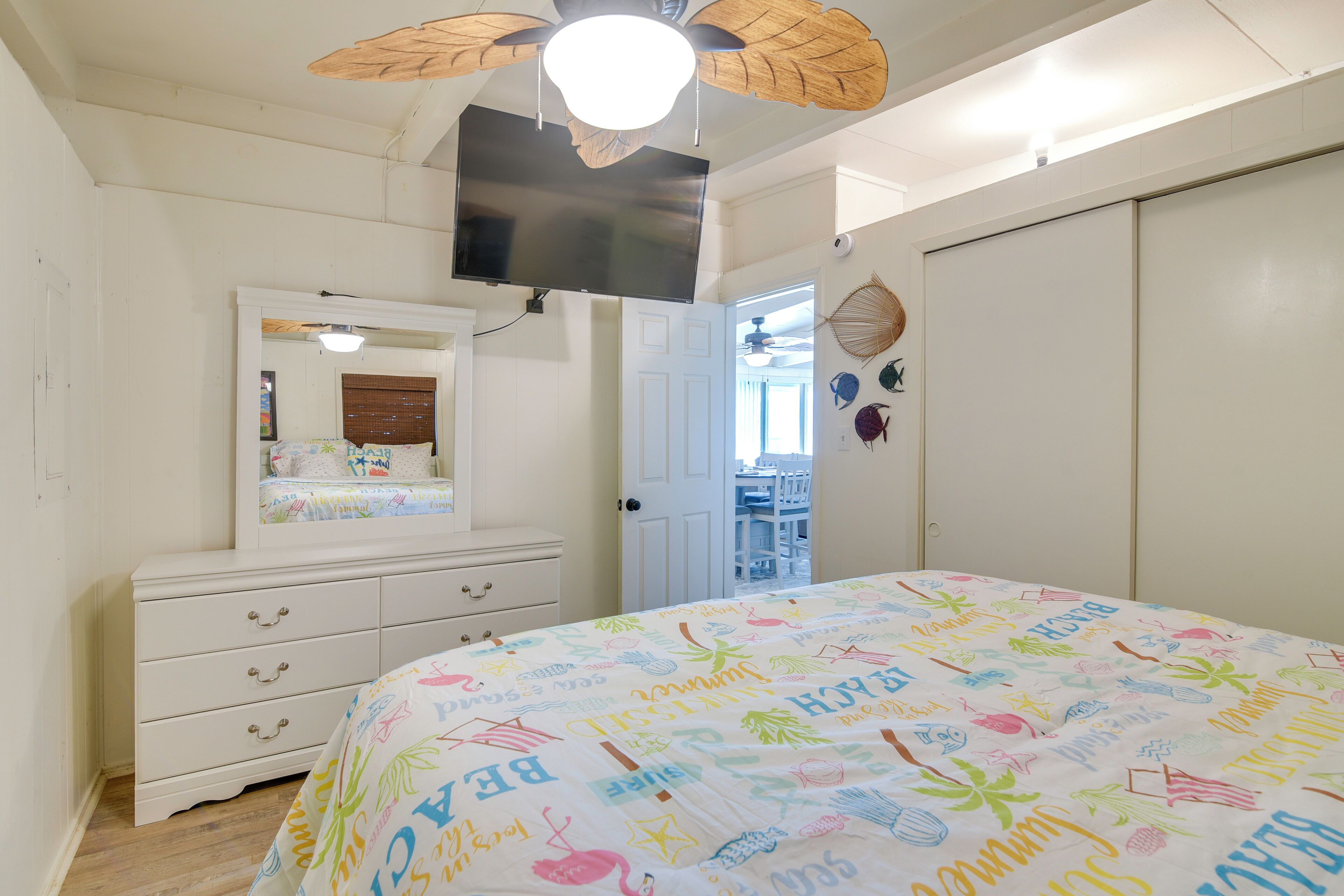 Un dormitorio con cama, cómoda, televisor y puerta que da a un balcón.