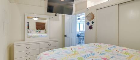 Un dormitorio con cama, cómoda, televisor y puerta que da a un balcón.