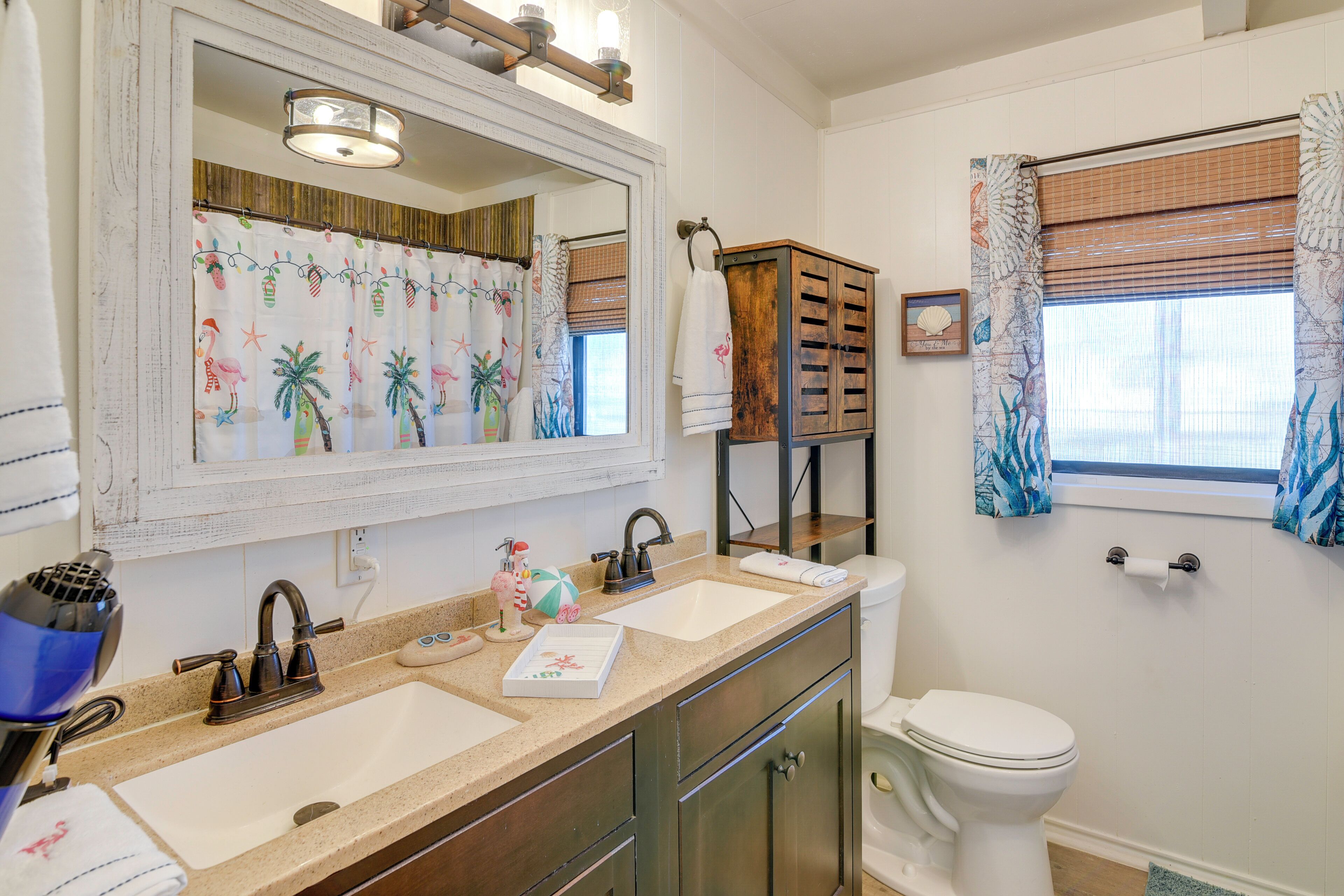 A bathroom with two sinks, a toilet, a mirror, and a window with curtains.