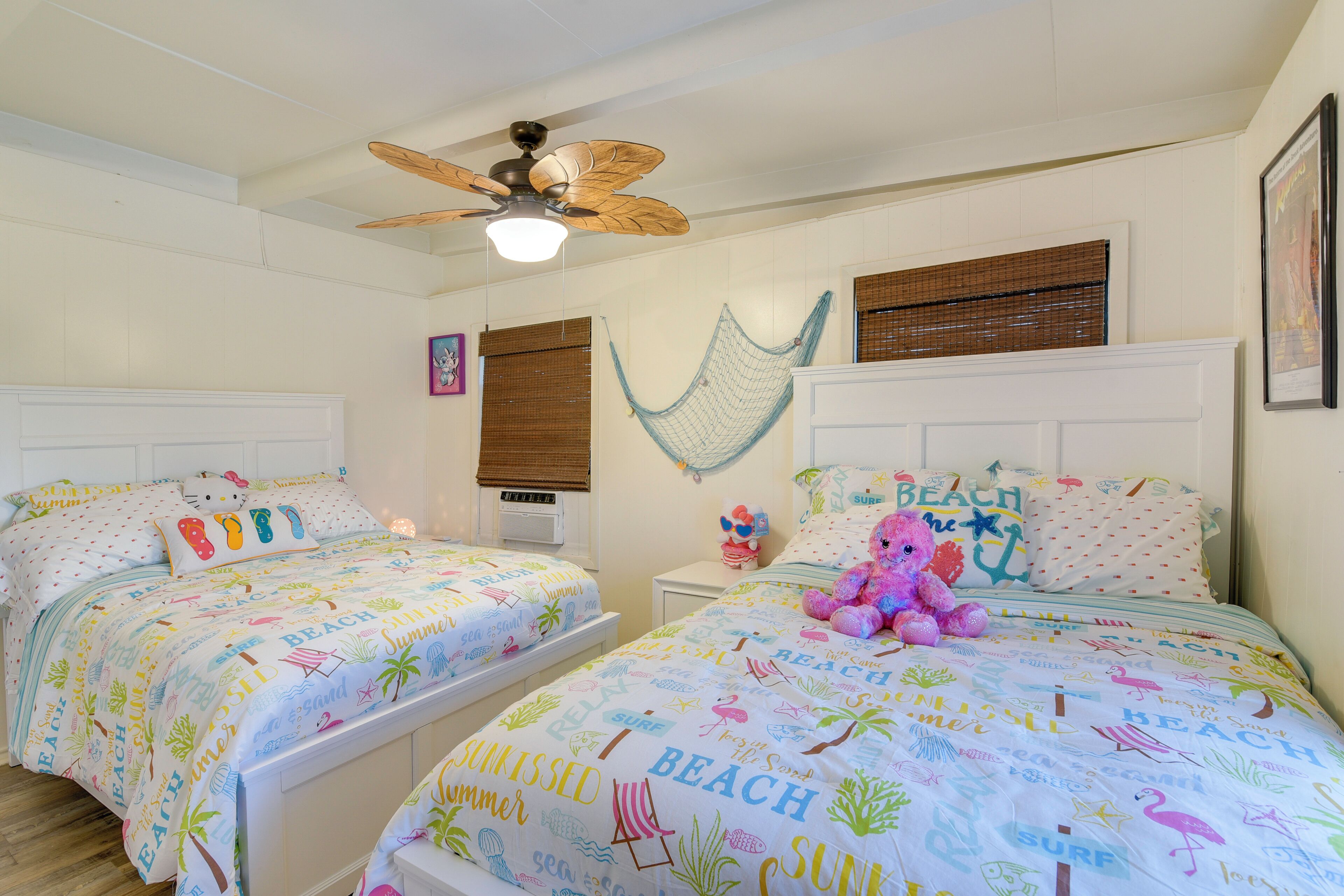 Une chambre avec deux lits, un ventilateur de plafond, un hamac et du linge de lit sur le thème de la plage.