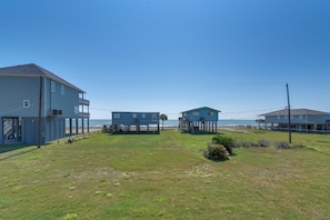 A coastal property with a large building, a smaller house on stilts, and a grassy area. - Steps to Surfside Beach! Ocean-view Texas Retreat (Freeport)
