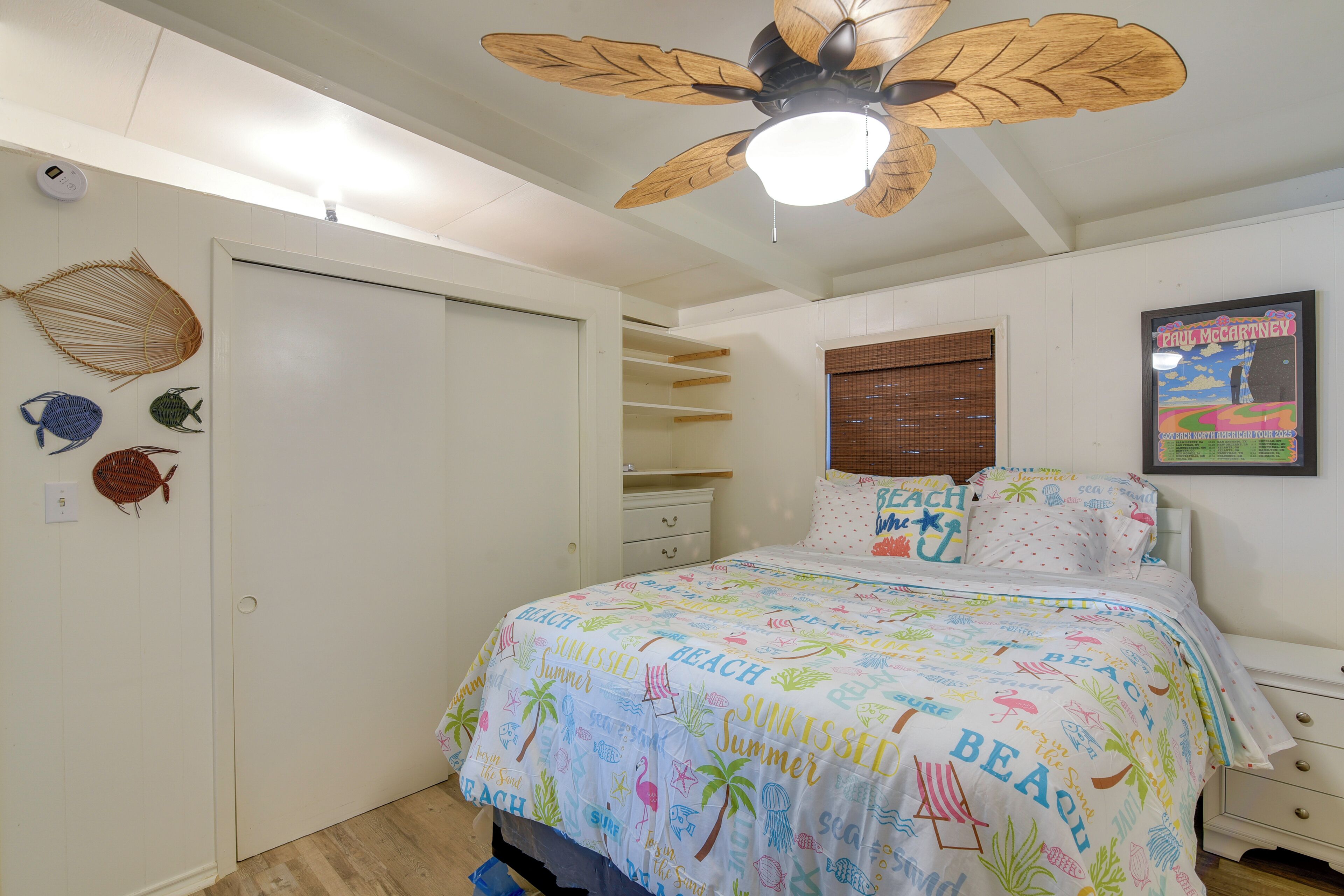 Une chambre à coucher avec un lit, un ventilateur de plafond, une horloge murale et une affiche.