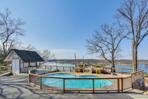 A swimming pool with a wooden deck and a small building, surrounded by trees and a view of a body of water. - Bagnell Strip Studio for Shootout Weekend Fun (Lake Ozark)