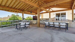 Un patio al aire libre con techo de madera, piso de concreto y sillas blancas.