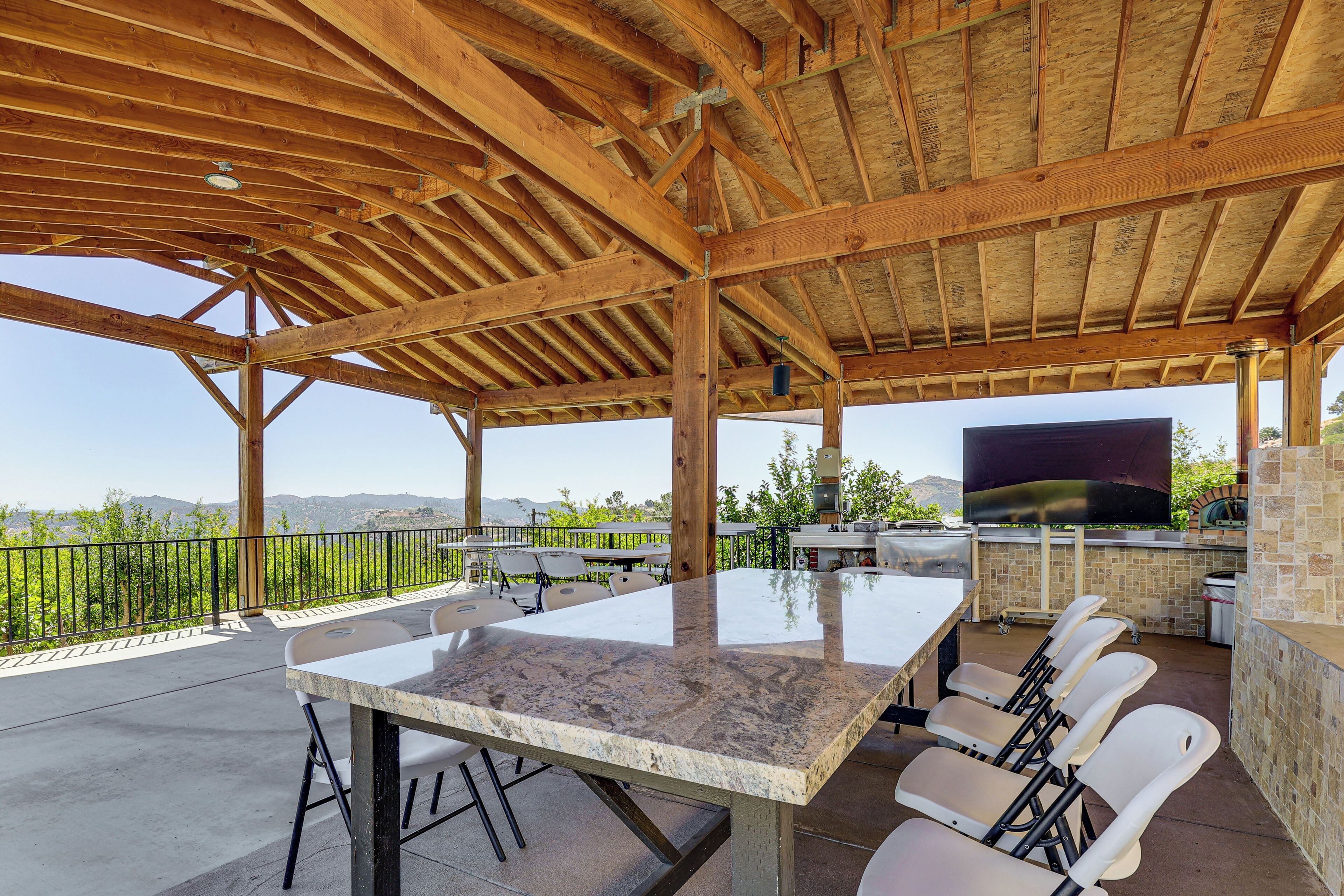 An outdoor patio with a large table, chairs, a grill, and a TV.