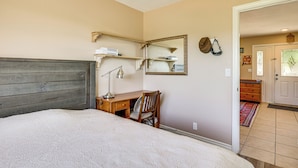 Un dormitorio con cama, escritorio, silla, lámpara de escritorio, espejo y cómoda.