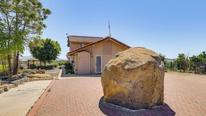 Una casa con una roca grande al frente, un sendero pavimentado y un área cercada con árboles.
