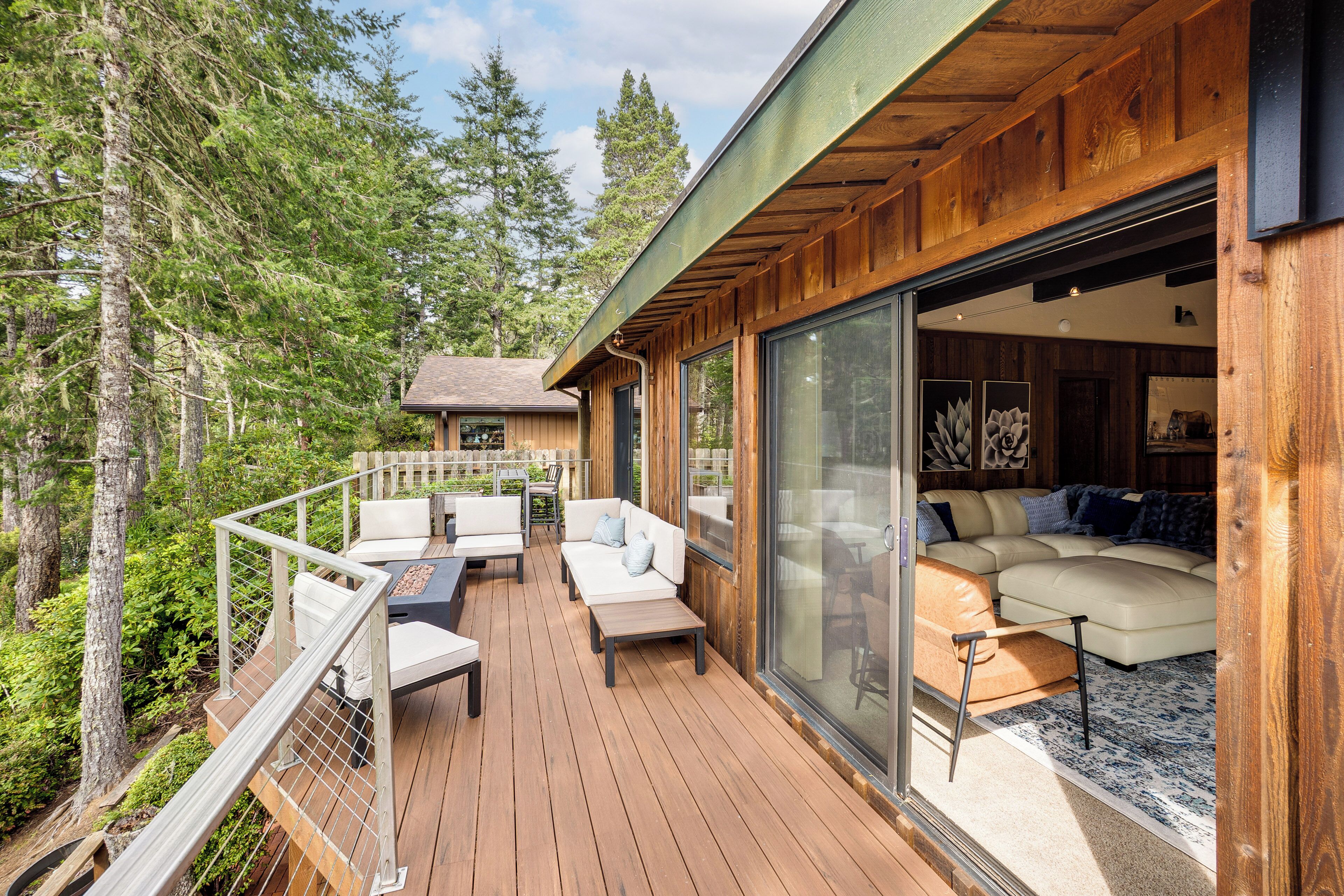 A wooden deck with outdoor furniture, a glass door leading to an interior with a sofa and cushions.
