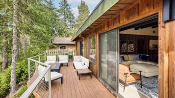A wooden deck with outdoor furniture, a glass door leading to an interior with a sofa and cushions.