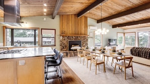 Una cocina amplia con una isla central, comedor con sillas de madera, chimenea y ventanas grandes.
