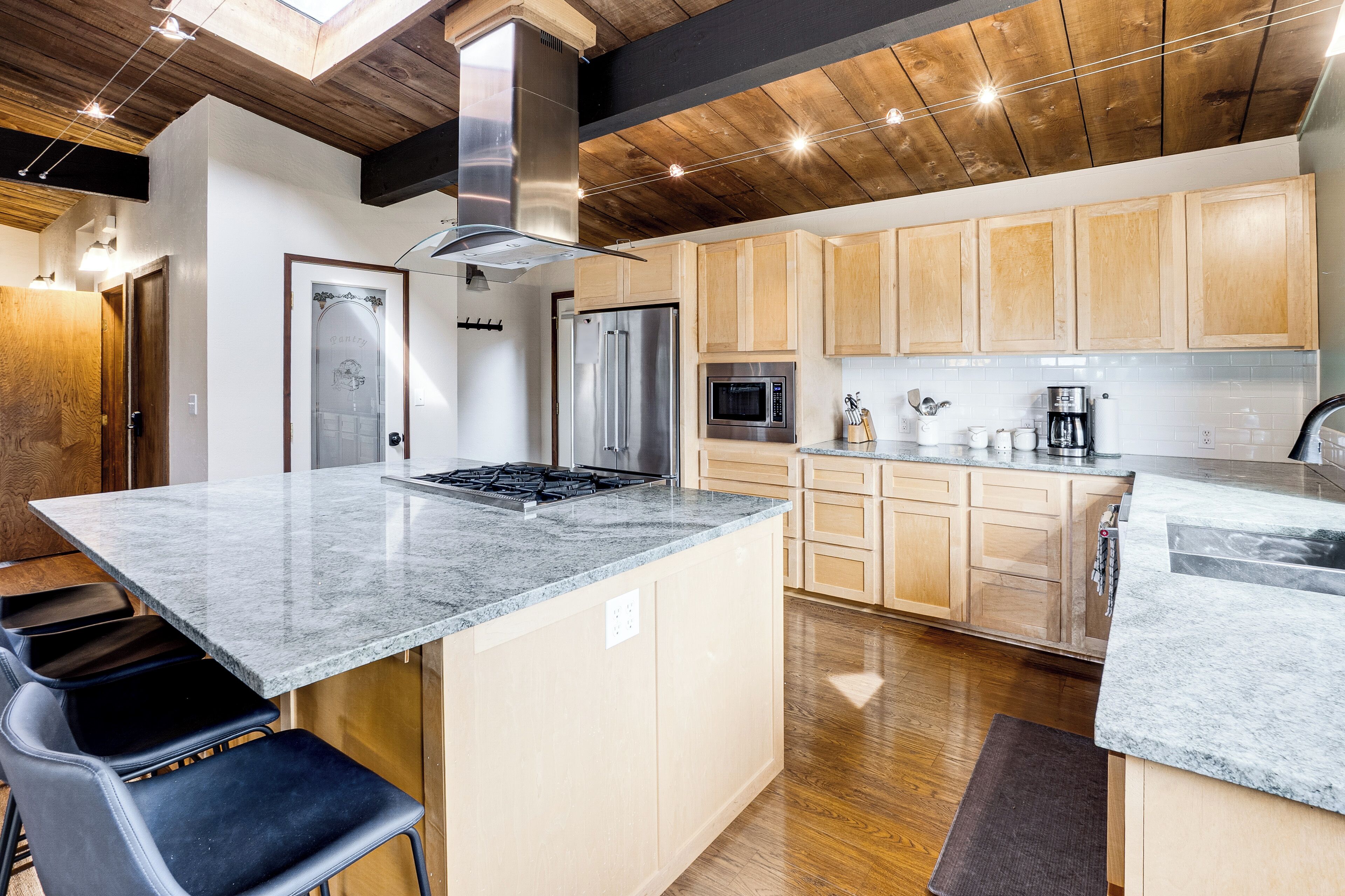 A modern kitchen with wooden cabinets, a central island, stainless steel appliances, and a bar area.