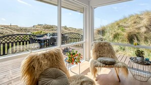 A sunlit room with a view of dunes, a wooden deck, and a dining area with outdoor furniture. - 4 Star Holiday Home in Saltum (Saltum)