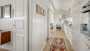 A hallway with white paneling, a wooden bench, framed pictures, and a patterned rug. - 4 Star Holiday Home in Saltum (Saltum)