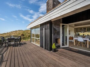 A modern house with a deck, a dining area, and a kitchen visible through glass doors. - 4 Star Holiday Home in Saltum (Saltum)