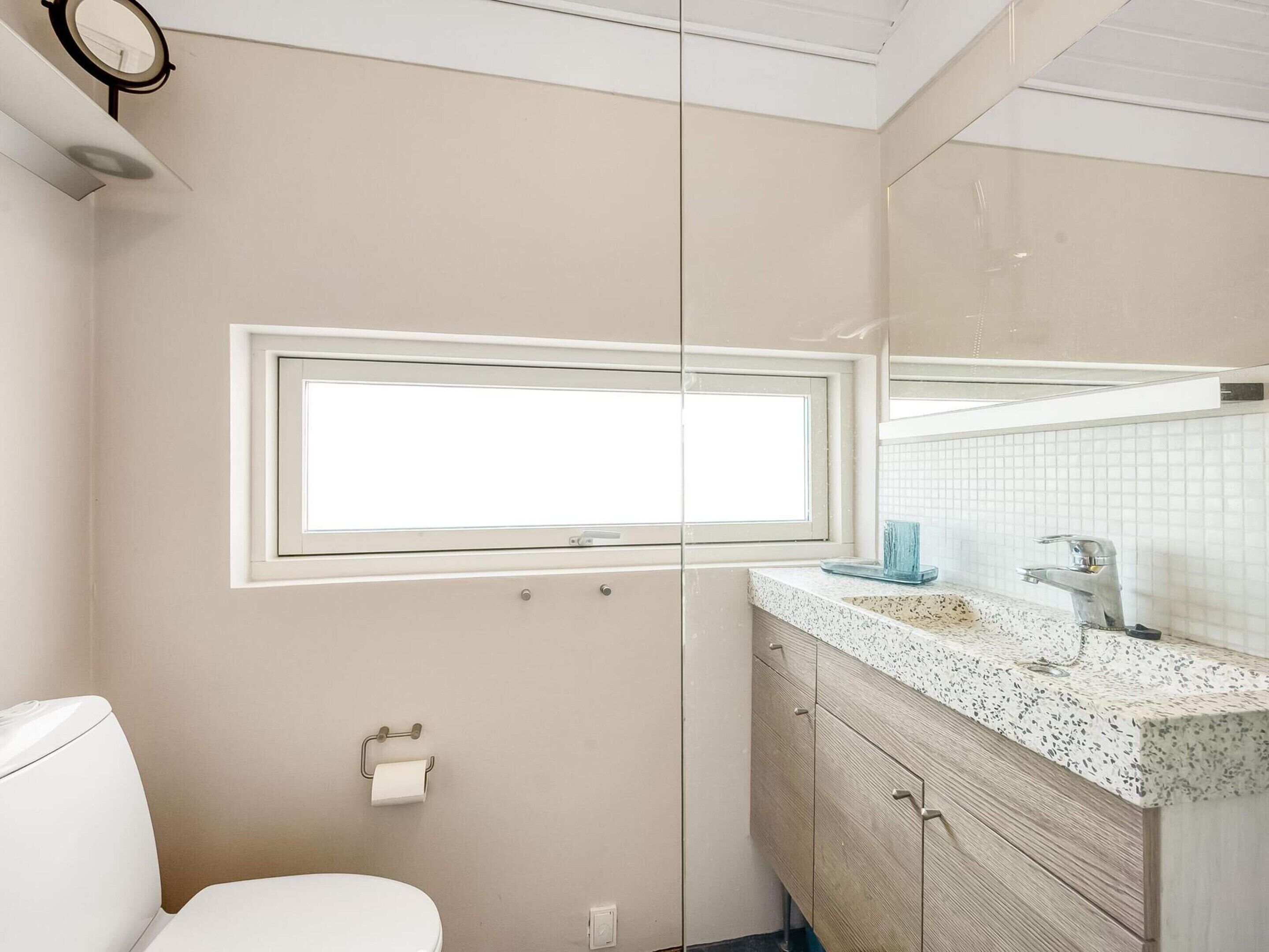 A bathroom with a toilet, a sink with a mirror, and a window.