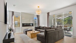 Een moderne woonkamer met een hoekbank, een flatscreen-tv, een open haard en grote ramen.