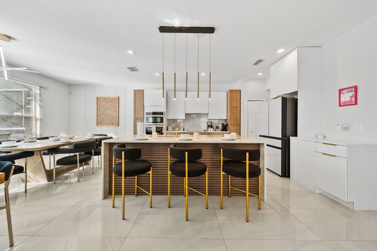 A modern kitchen with a central island, bar stools, and a dining area with a table and chairs.