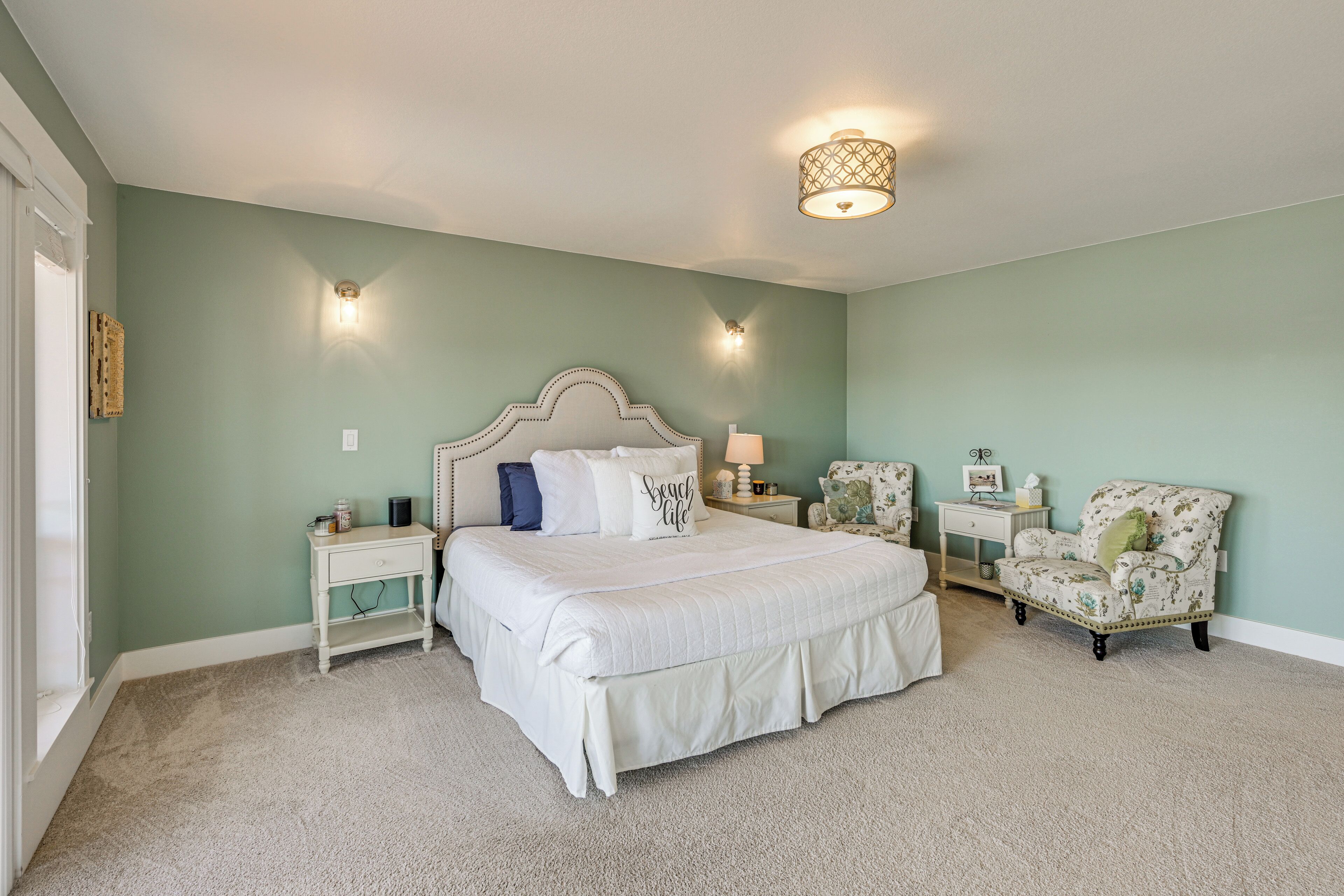 A bedroom with a large bed, two bedside tables, a nightstand, a chair, and a wall-mounted light fixture.