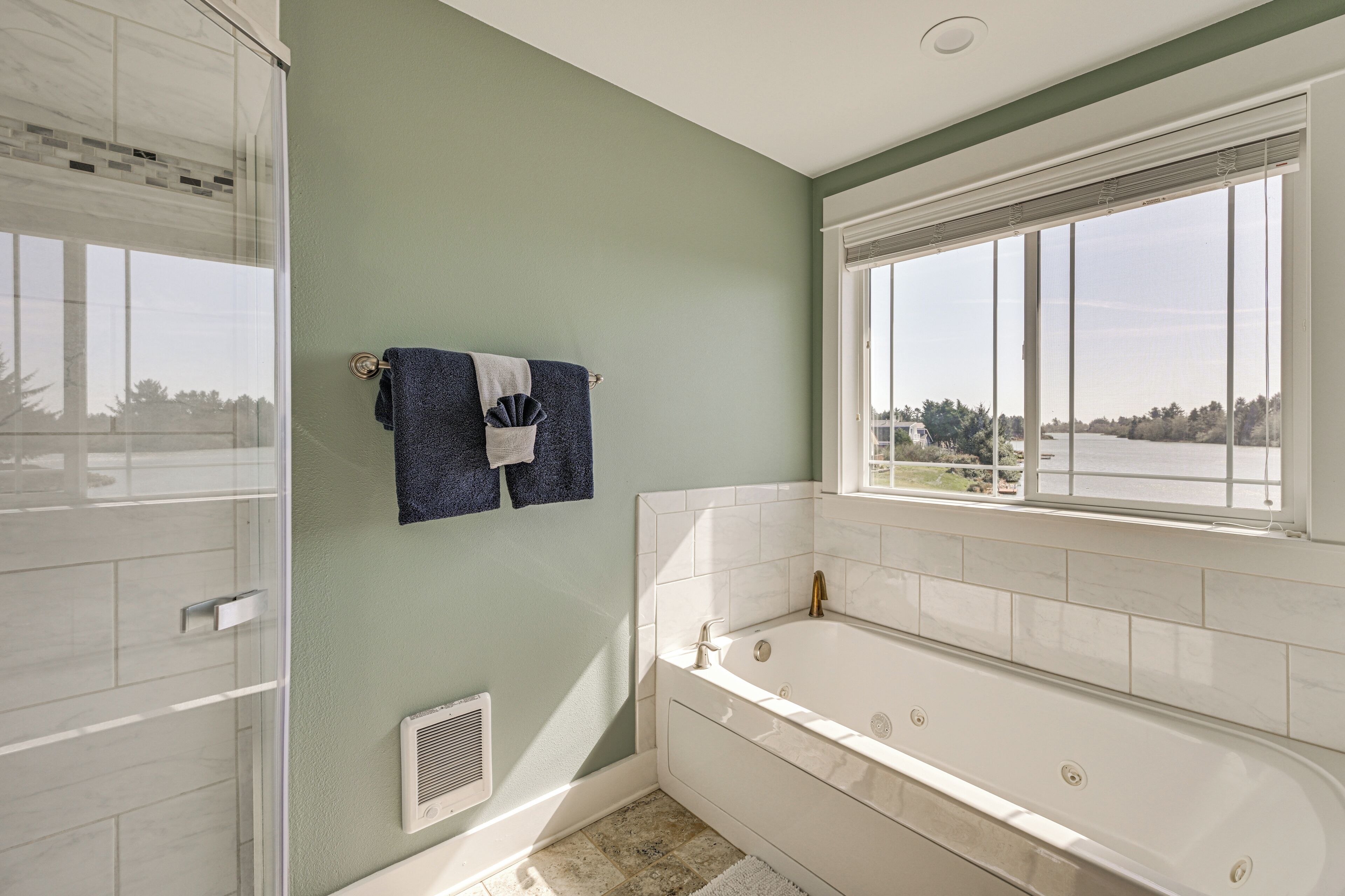 A bathroom with a bathtub, a shower, a window with a view, and a towel rack.