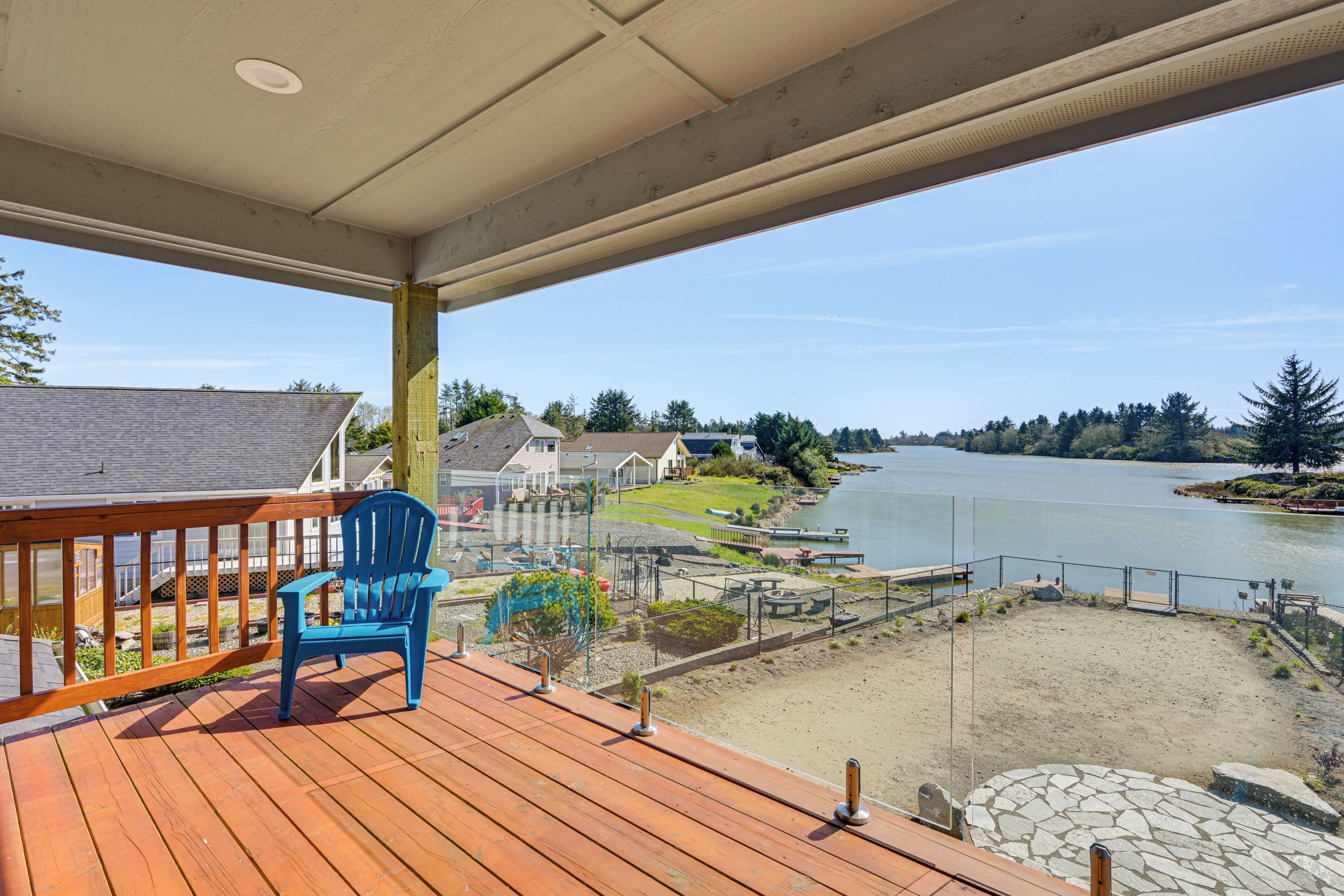 A wooden deck with a blue chair, overlooking a lake with houses and greenery in the background.