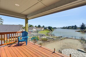 Una terraza de madera con una silla azul, con vistas a un lago y casas, rodeado de vegetación.