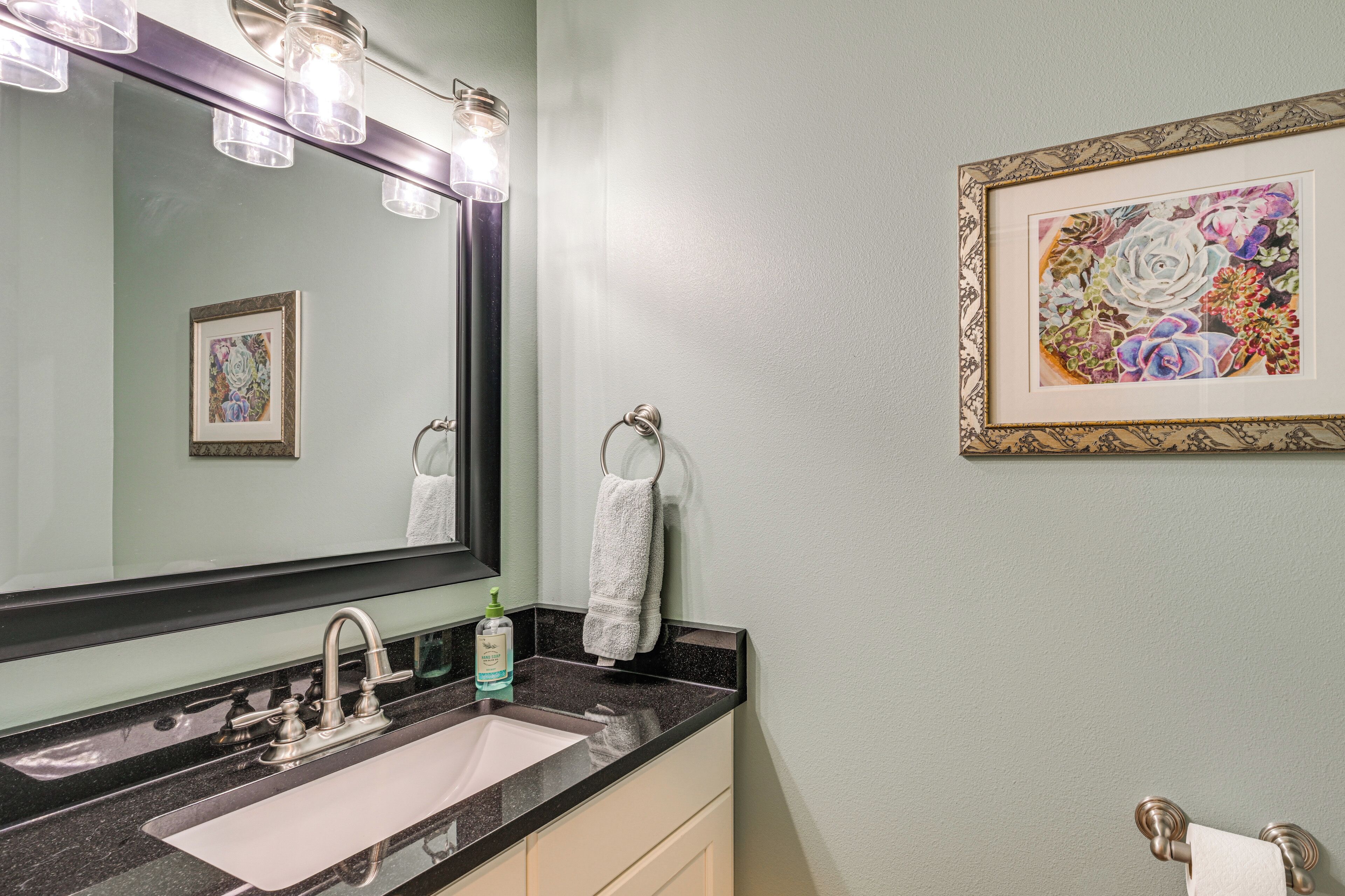 A bathroom with a sink, mirror, towel rack, and framed artwork on the wall.