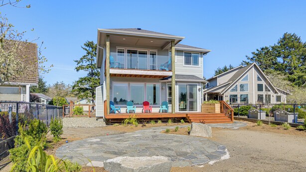 A two-story house with a balcony, a stone patio, and a fenced yard. - Lakefront Getaway w/ Private Dock in Ocean Shores! (Ocean Shores)