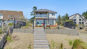 A two-story house with a front porch, a fenced yard, and a staircase leading to the entrance. - Lakefront Getaway w/ Private Dock in Ocean Shores! (Ocean Shores)