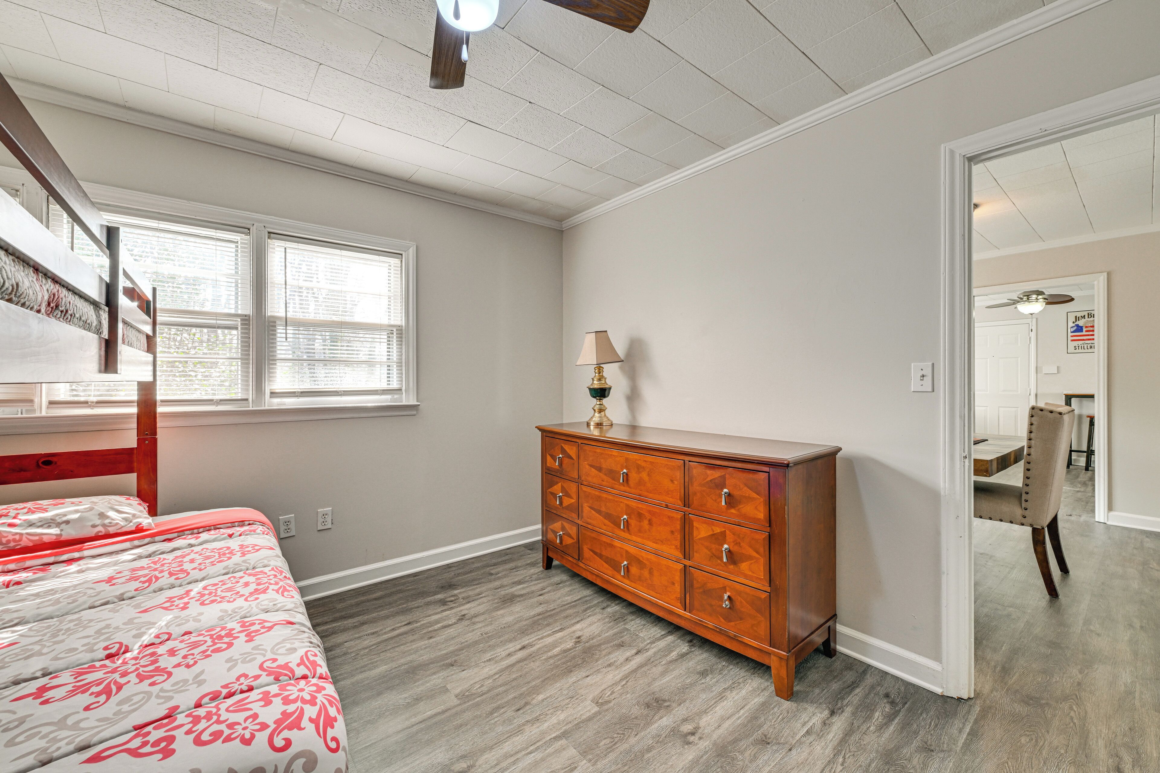 A bedroom with a bed, dresser, window, and a door leading to another room.