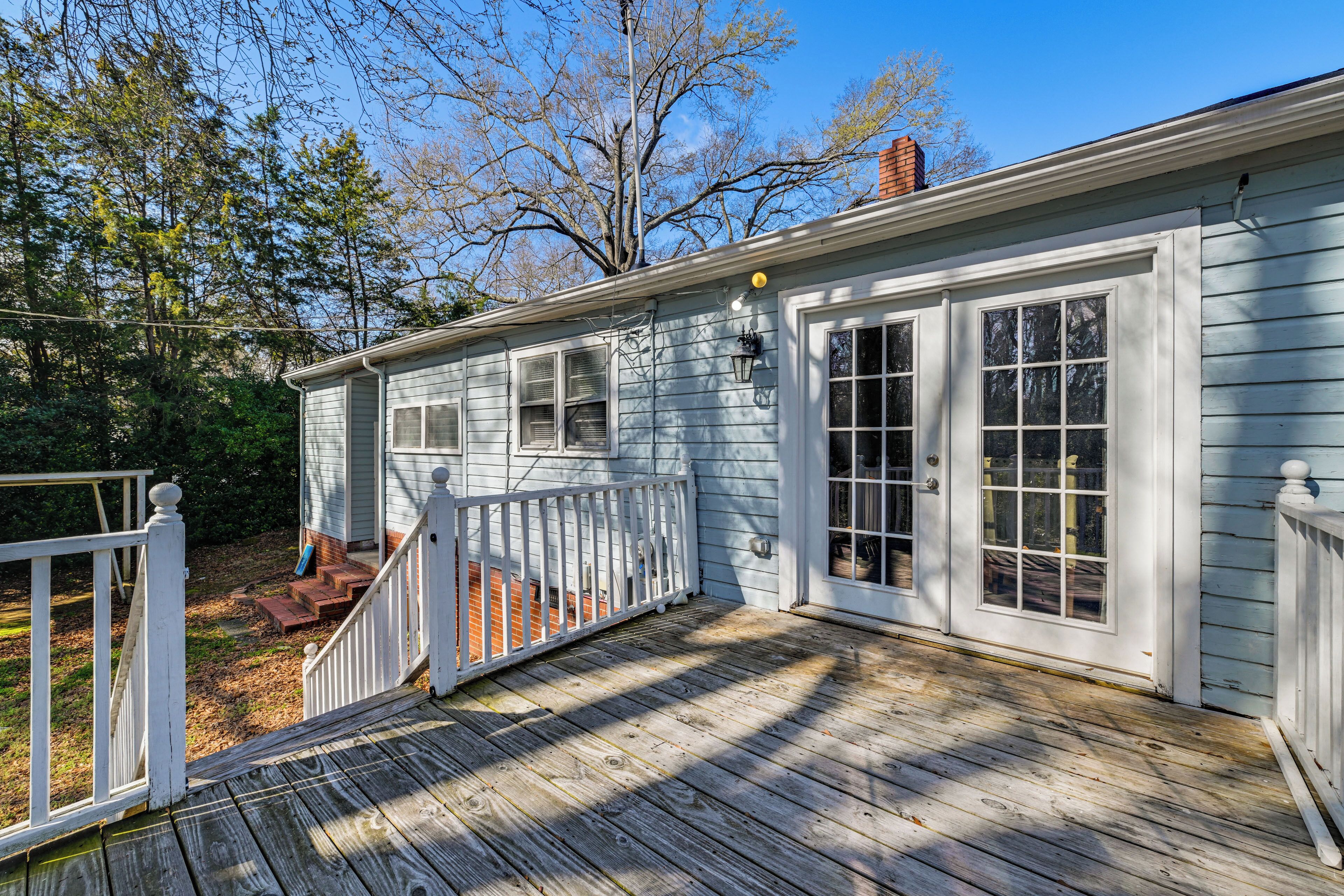 A wooden deck with a white railing, a brick pathway, and a house with white siding and large windows.