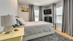Ein modernes Schlafzimmer mit Bett, Nachttisch, Lampe und einem angebrachten Fernseher.