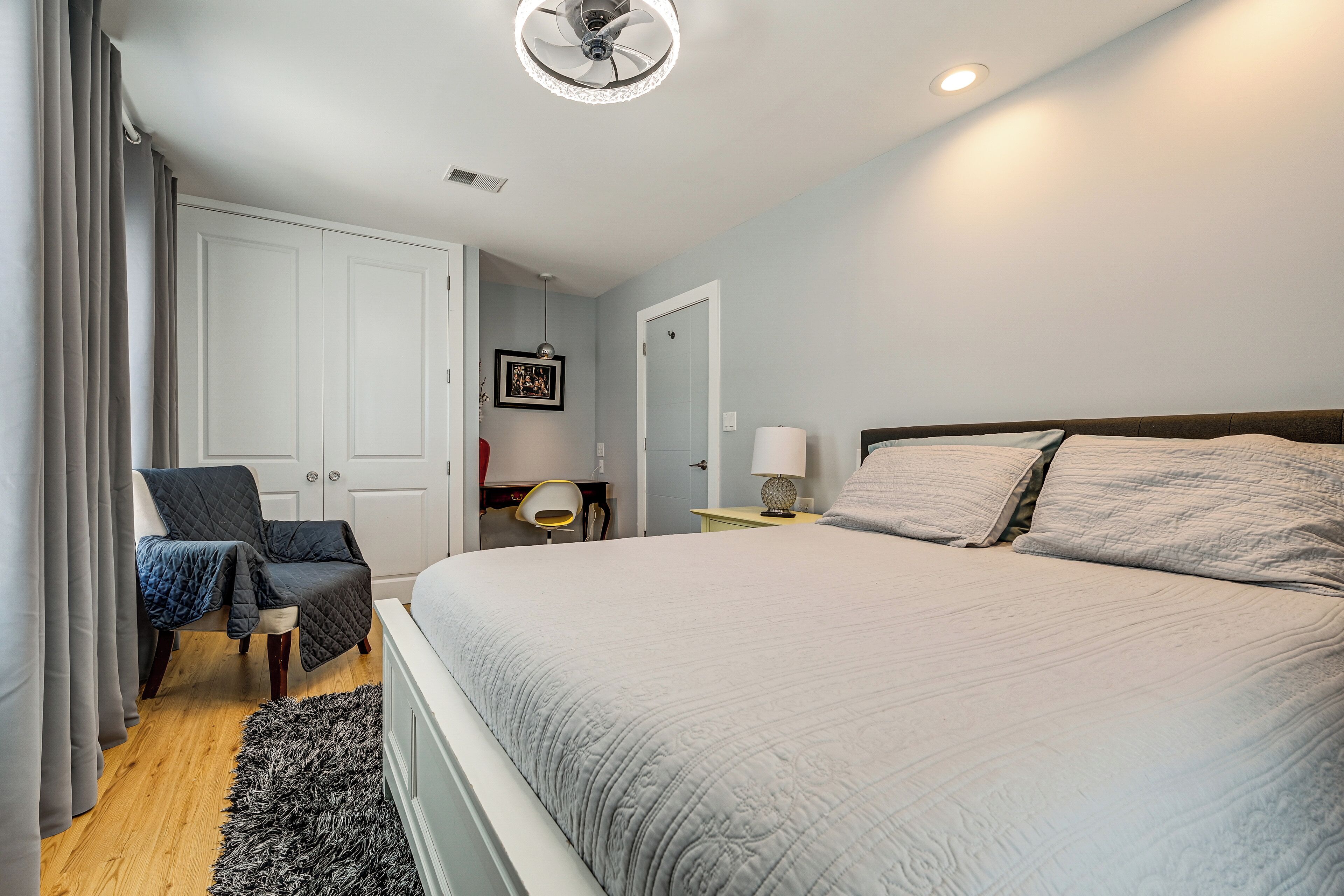 A bedroom with a bed, a chair, a desk, and a door.