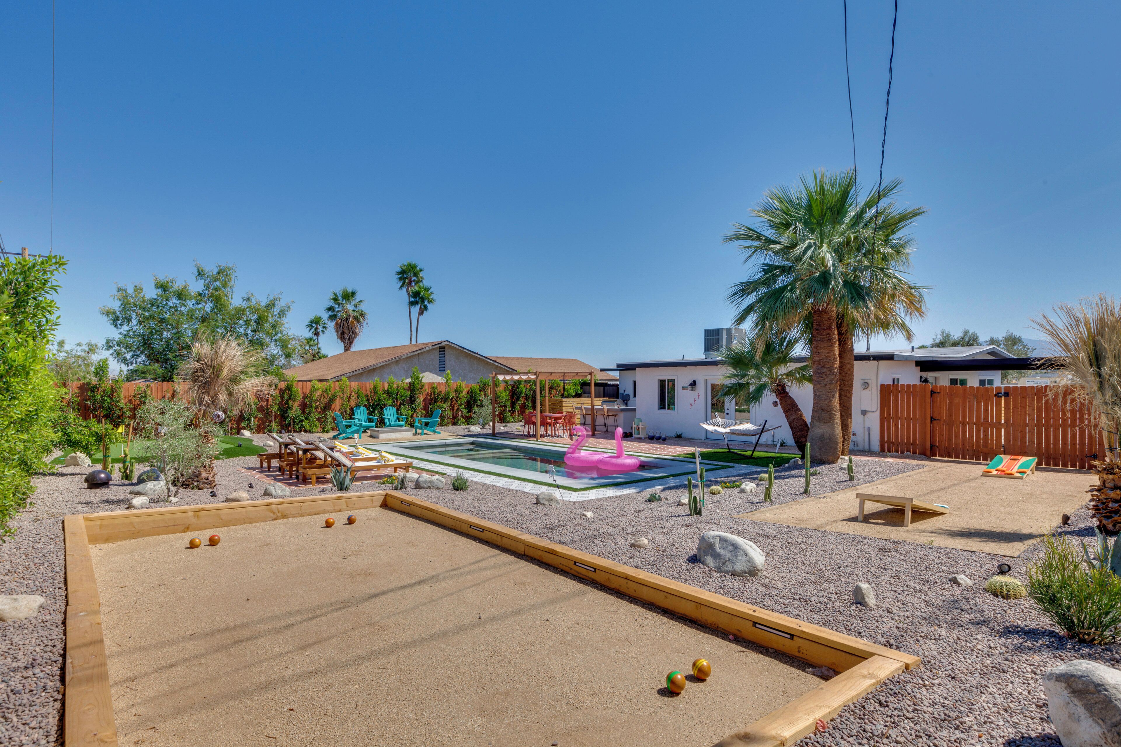 A backyard with a pool, a bocce court, and a wooden deck.