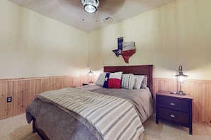 Ein Schlafzimmer mit hölzernem Kopfteil, einem Bett mit gestreifter Bettwäsche, zwei Nachttischen mit Lampen und einer Wanddekoration mit der Texas-Flagge.