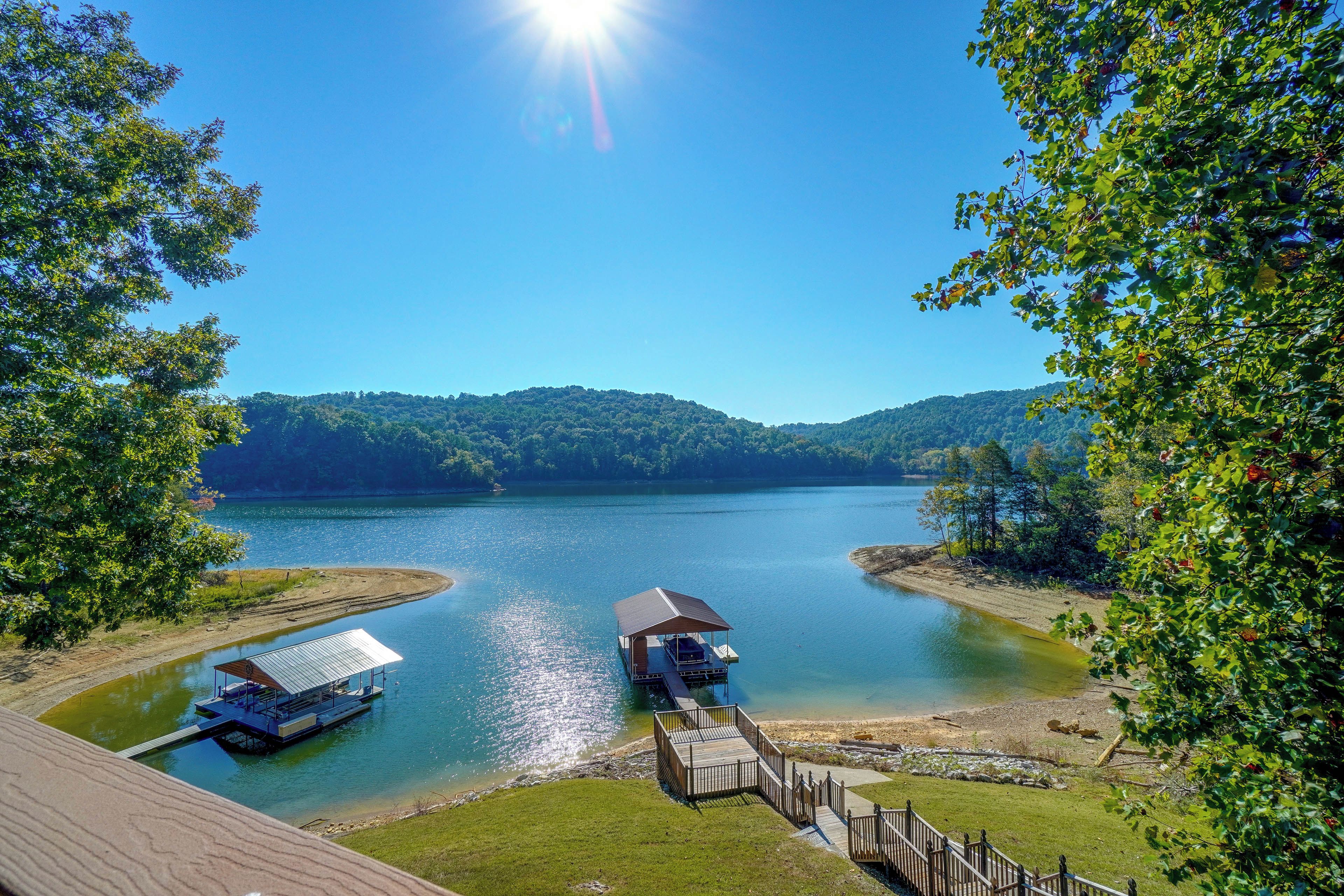 A lakeside property with a dock, a covered boat launch, and a grassy area leading to a wooden deck.