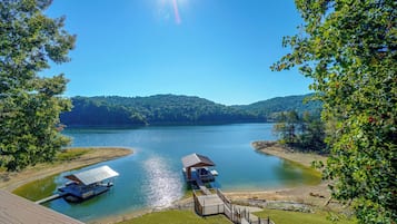 A lakeside property with a dock, a covered boat launch, and a grassy area leading to a wooden deck.