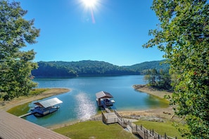 A lakeside property with a dock, a covered boat launch, and a grassy area leading to a wooden deck. - Hot Tub + Dock! Waterfront Norris Lake Log Home (New Tazewell)