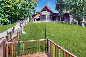 A modern lodge with a wooden deck leading to a stone entrance, surrounded by lush greenery. - Hot Tub + Dock! Waterfront Norris Lake Log Home (New Tazewell)